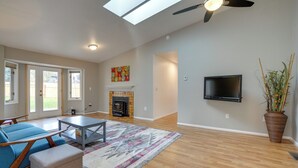 A spacious living room with a fireplace, a flat-screen TV mounted on the wall, and a large window allowing natural light. - Pet-friendly Anchorage Home - 8 Mi to Downtown! (Anchorage)
