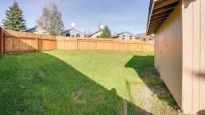 A backyard with a wooden fence, a shed, and houses in the background. - Pet-friendly Anchorage Home - 8 Mi to Downtown! (Anchorage)