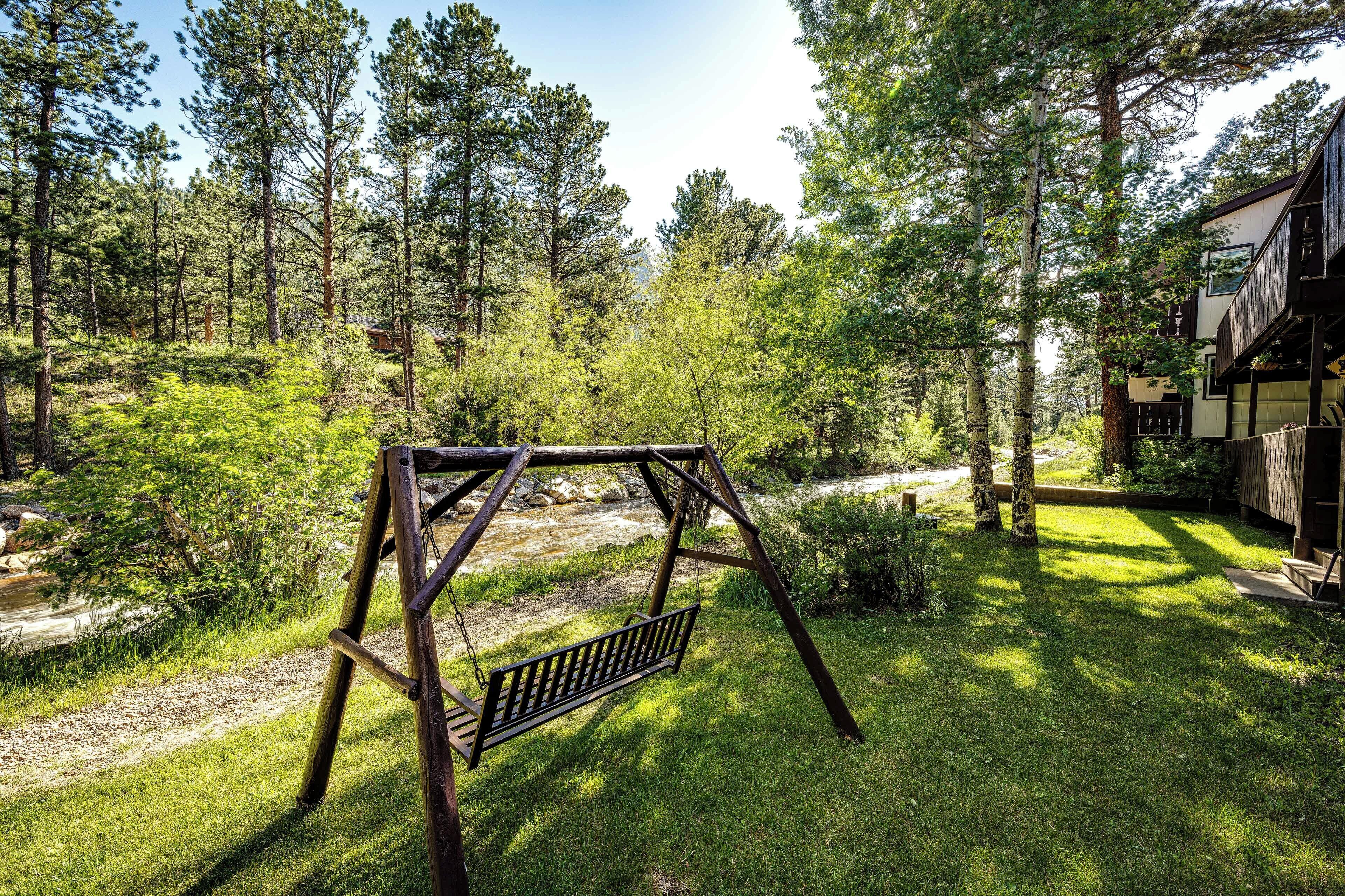 Un ensemble de balançoires en bois, installé dans une zone boisée, avec un bâtiment visible en arrière-plan.