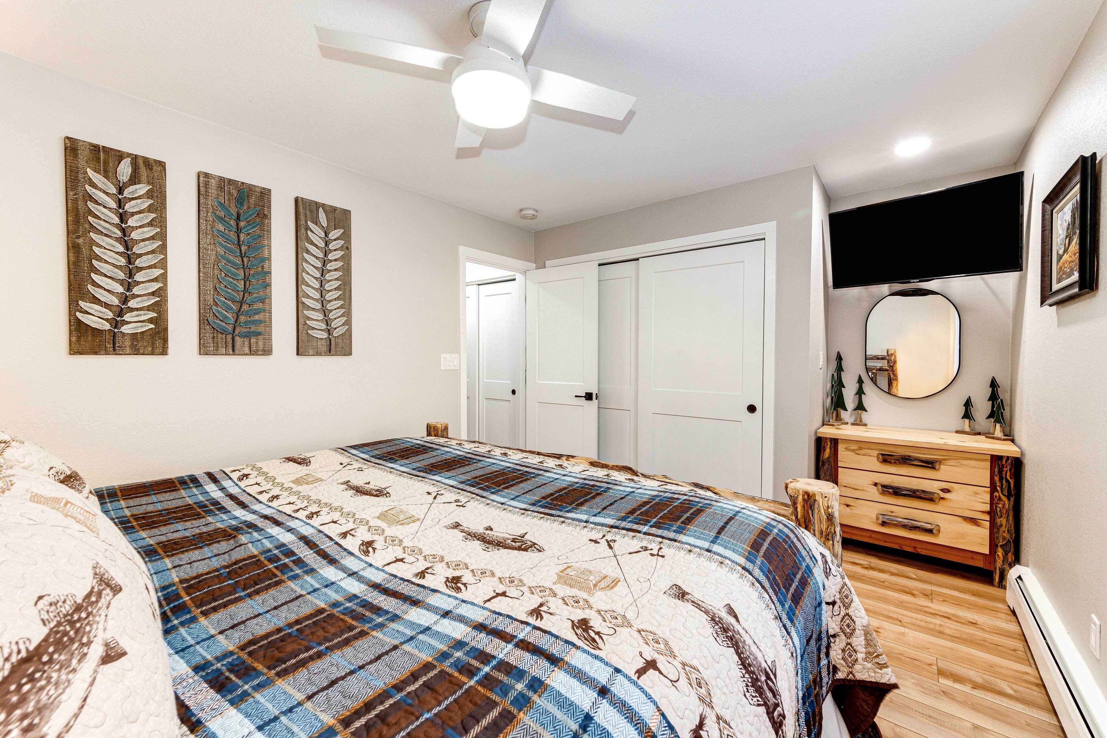 Une chambre à coucher avec un lit, une commode, un ventilateur de plafond et des œuvres d’art accrochées au mur.
