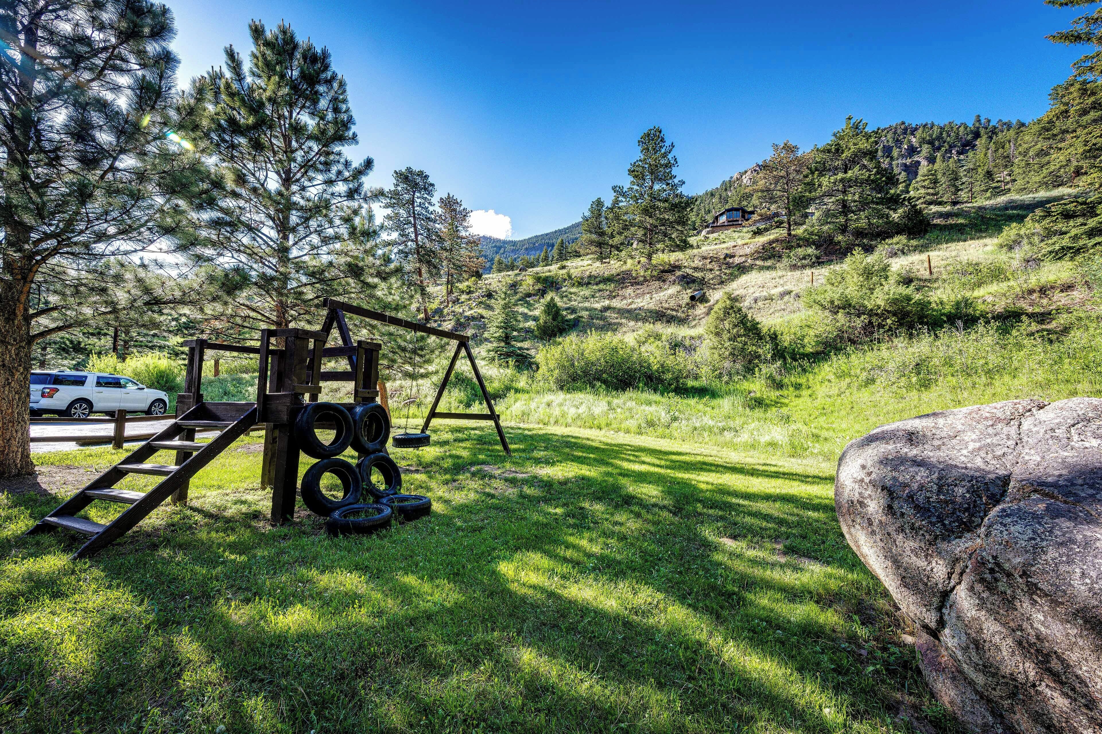 A grassy area with a wooden swing set and a large rock.