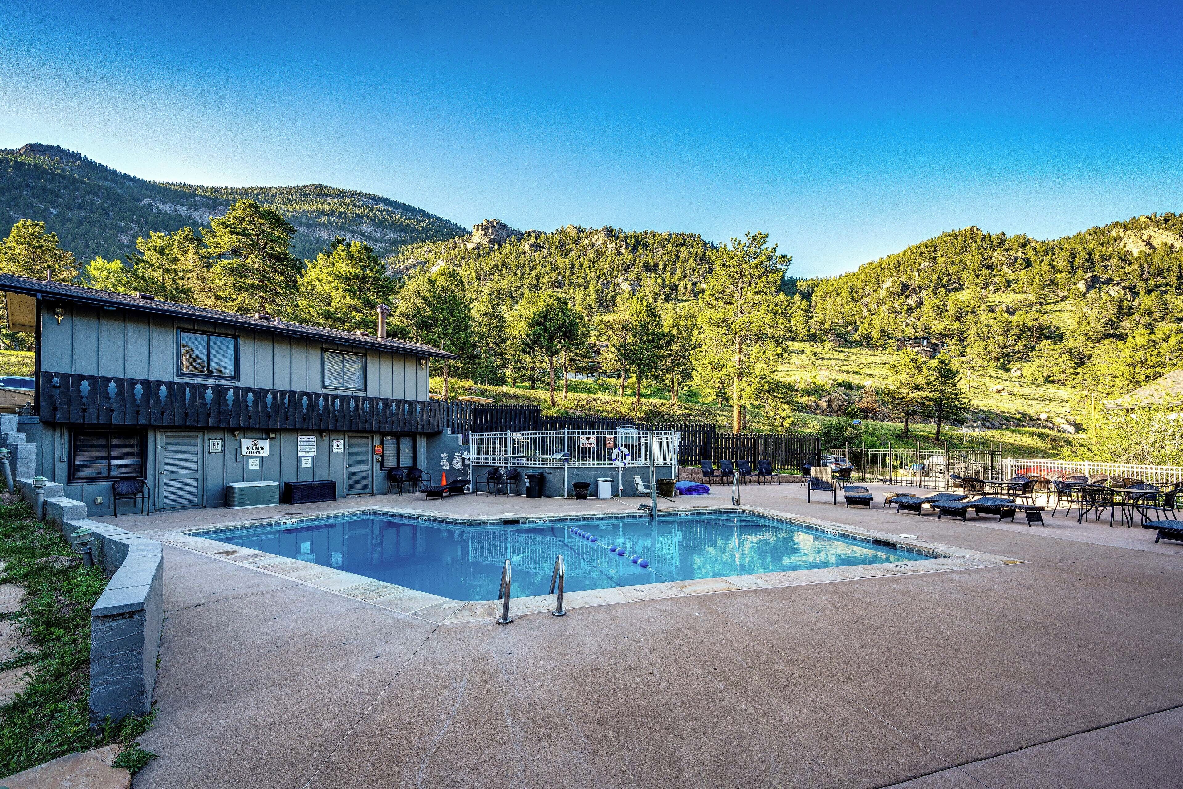 A pool area with a building, outdoor seating, and a mountainous backdrop.