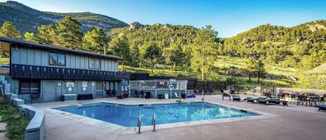 A pool area with a building, outdoor seating, and a mountainous backdrop.