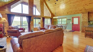 A spacious living room with a large leather sofa, wooden ceiling, and large windows offering a view of the outdoors. - Murphy Cabin w/ Hot Tub, Fire Pit & Mountain Views (Murphy)