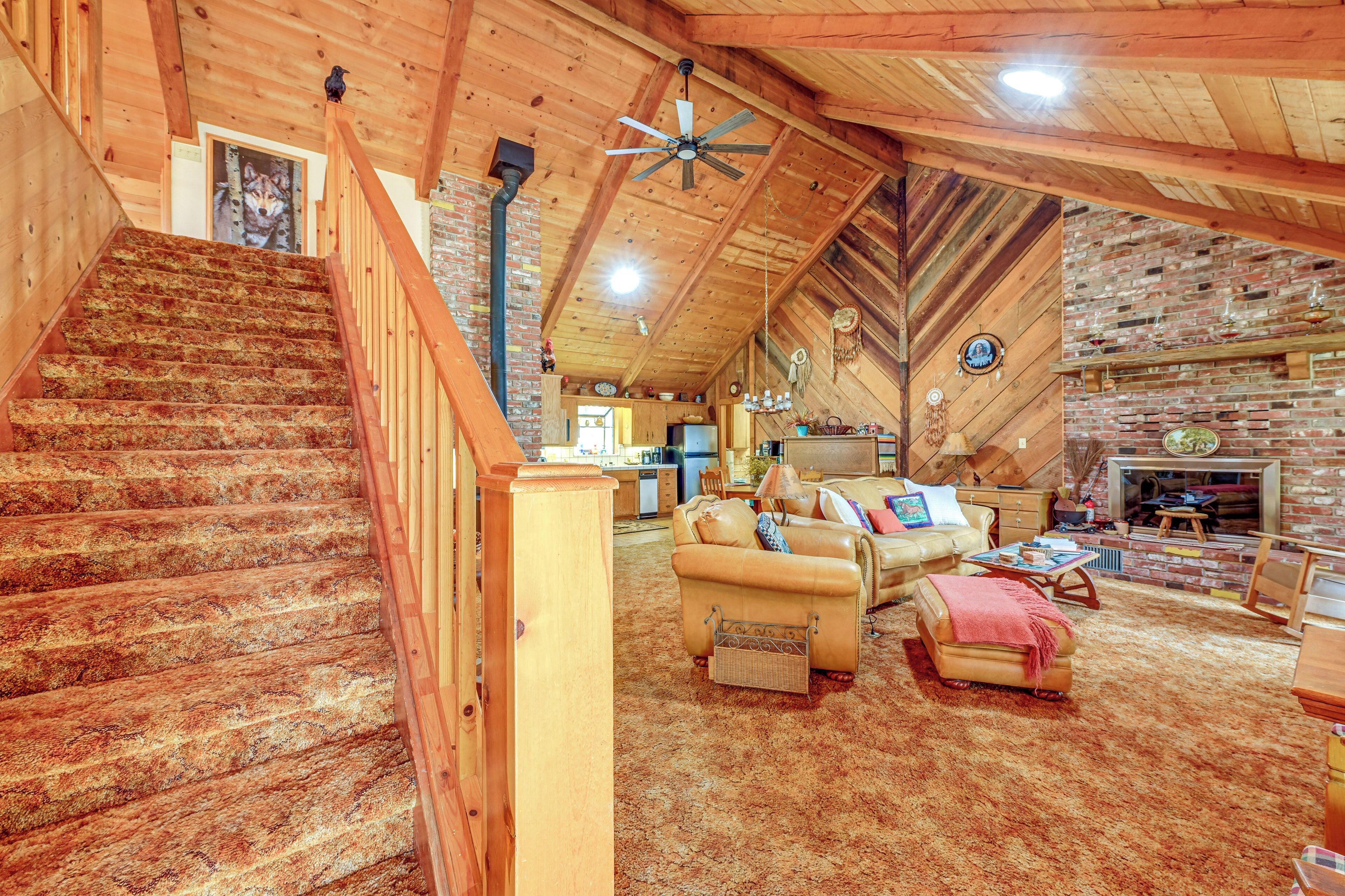 Um loft amplo com pé-alto, escada de madeira e uma sala de estar aconchegante com sofás de couro e lareira.