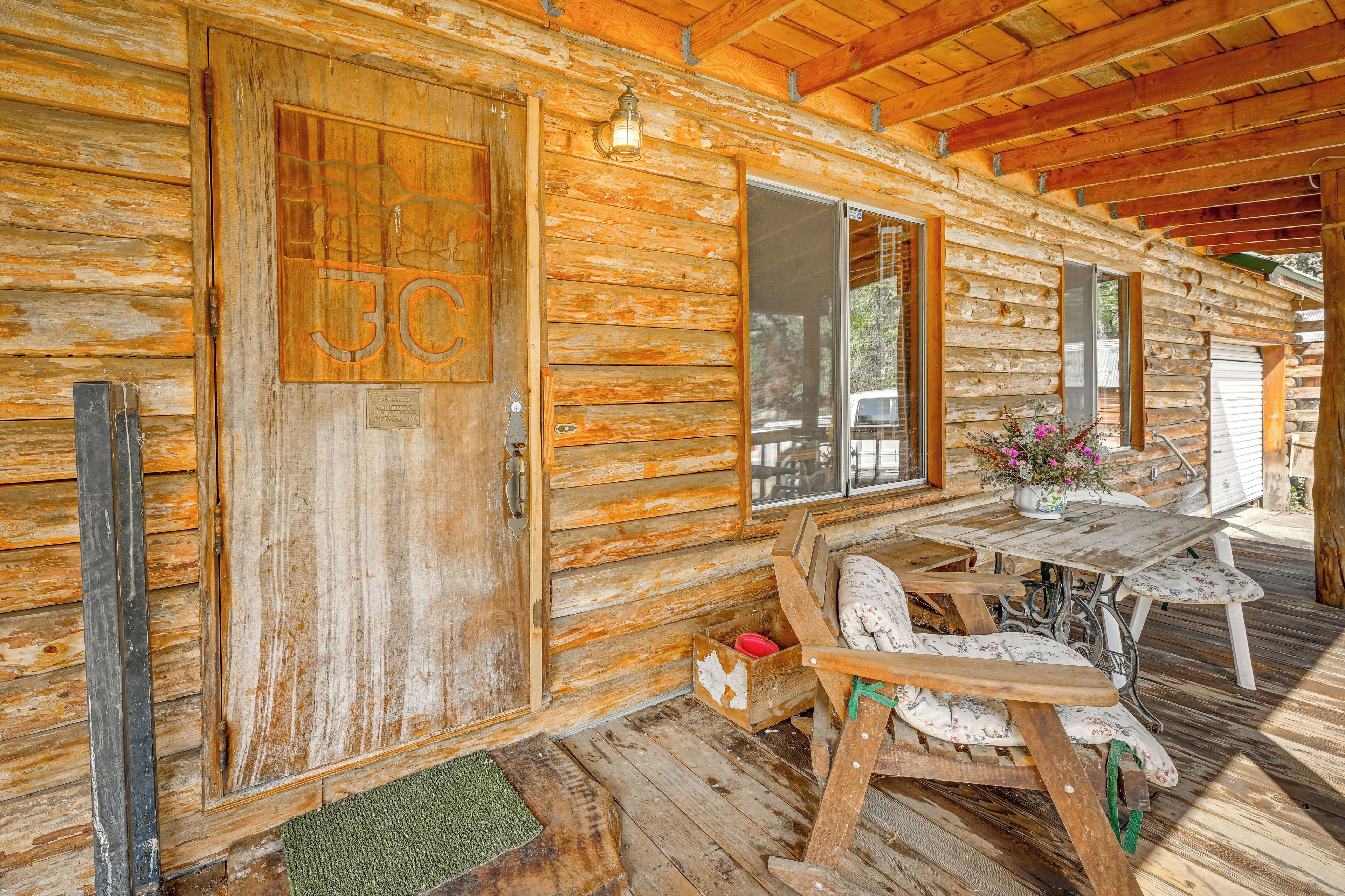 Une cabane rustique en bois, dotée d’une porte en bois, d’un banc et d’une table sur laquelle est posé un vase de fleurs.