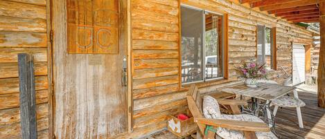 Une cabane rustique en bois, dotée d’une porte en bois, d’un banc et d’une table sur laquelle est posé un vase de fleurs.