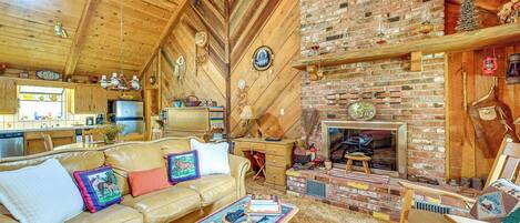 Interior acogedor de una cabaña con techo de madera, chimenea de ladrillo, sofá de cuero y zona de comedor.