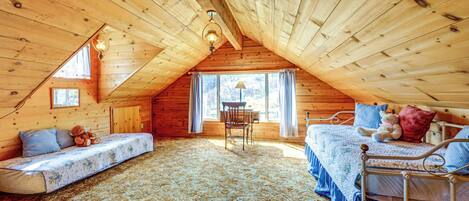 A cozy attic bedroom with a loft bed, a daybed, and a small table.