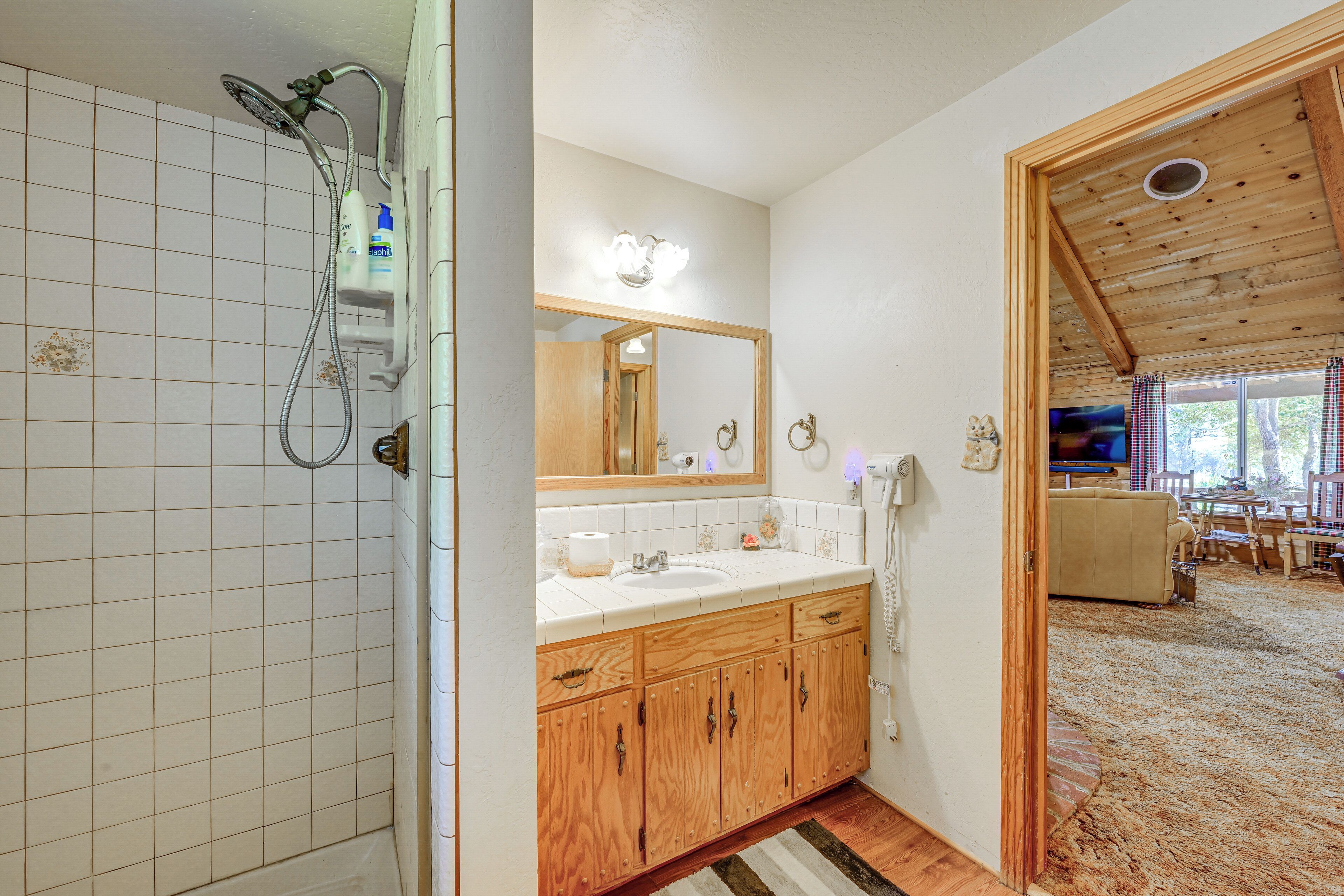 A bathroom with a shower, wooden cabinets, a sink, and a mirror.