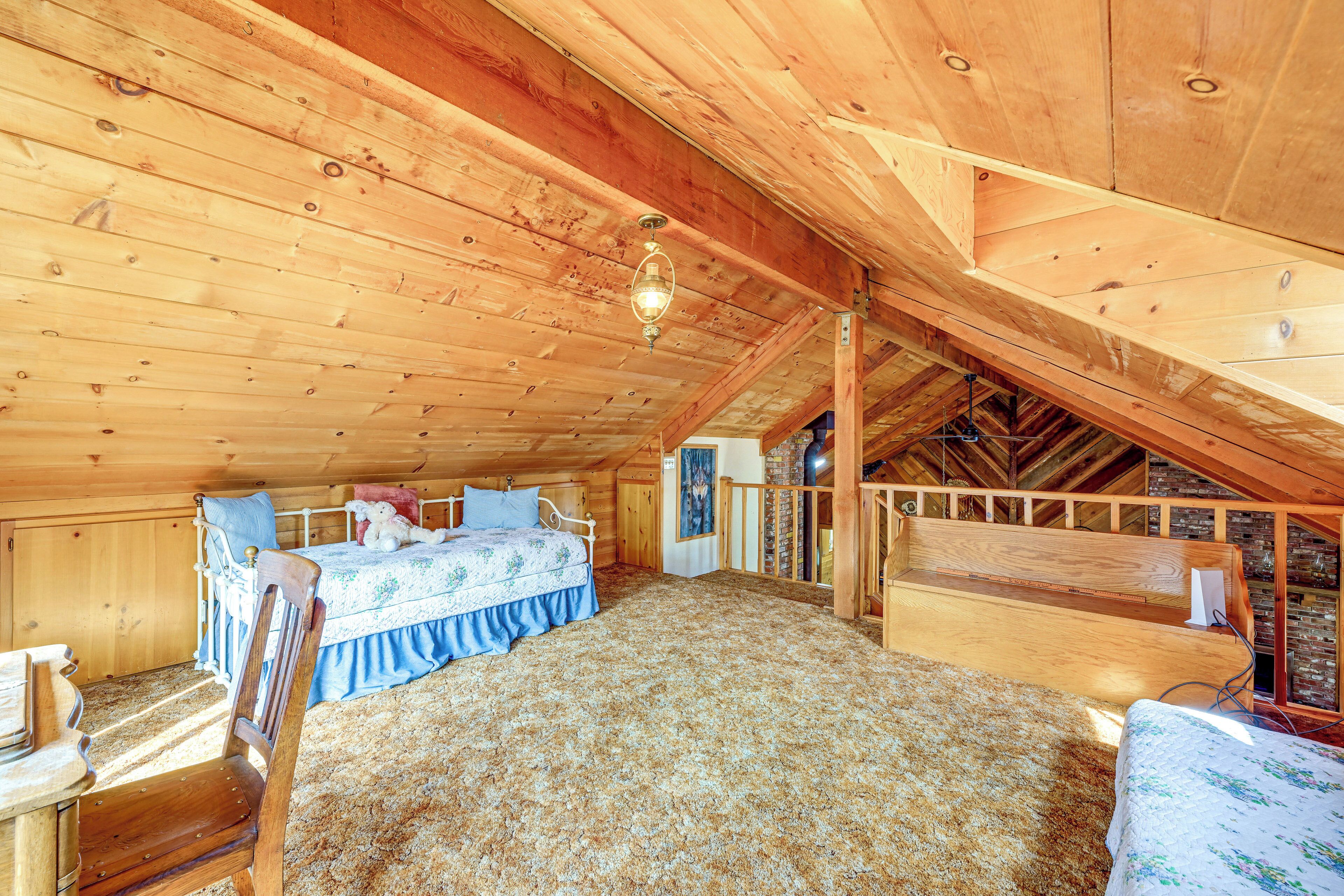 A cozy attic bedroom with a wooden ceiling, a bed with a floral bedspread, a chair, and a small table.
