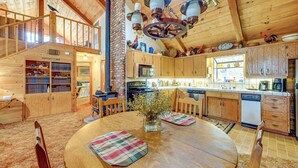 Una cocina amplia con armarios de madera, pared de ladrillo y comedor con una mesa redonda y manteles individuales a cuadros.