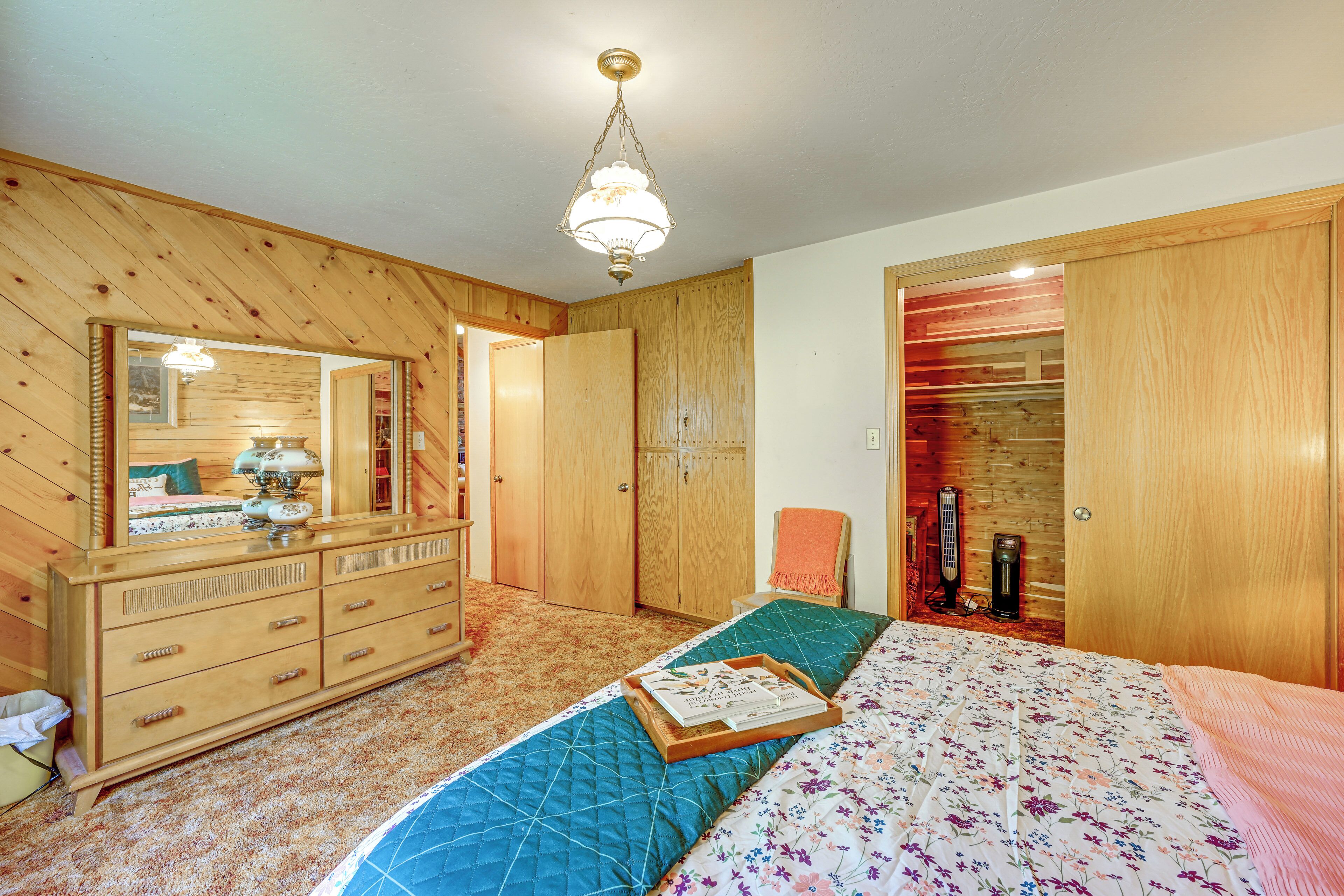 A bedroom with wooden walls, a bed with floral bedding, a dresser, a mirror, and a ceiling light.