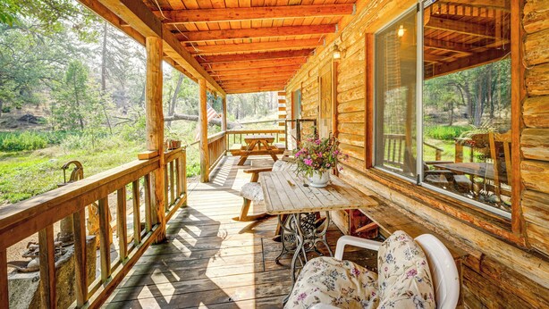 Una cabaña de madera con porche cubierto, mesa de picnic y zona de estar.