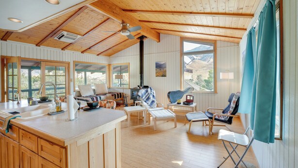A spacious living area with wooden flooring, a central island with a sink, and multiple seating options including a sofa and chairs. - Scenic Kernville Getaway w/ Deck & Mountain Views! (Kernville)
