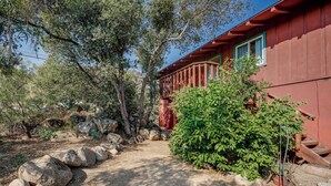 A red building with a wooden deck, surrounded by rocks and greenery. - Scenic Kernville Getaway w/ Deck & Mountain Views! (Kernville)