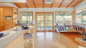 A cabin interior with wooden walls, a kitchen area, a bed, and large windows. - Scenic Kernville Getaway w/ Deck & Mountain Views! (Kernville)
