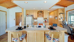 A kitchen with wooden cabinets, a central island with bar stools, a refrigerator, an oven, and a coffee machine. - Scenic Kernville Getaway w/ Deck & Mountain Views! (Kernville)
