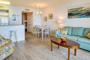 A modern living room with a sofa, a coffee table, and a dining area with chairs and a table. - Balcony & Beach Access: Oceanfront PCB Condo (Panama City Beach)