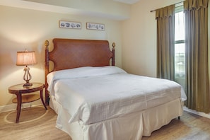 A neatly made bed in a room with a wooden headboard, a bedside table with a lamp, and two framed botanical prints on the wall.