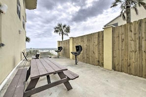 Un patio con un tavolo e sedie di legno, un barbecue e una palma.
