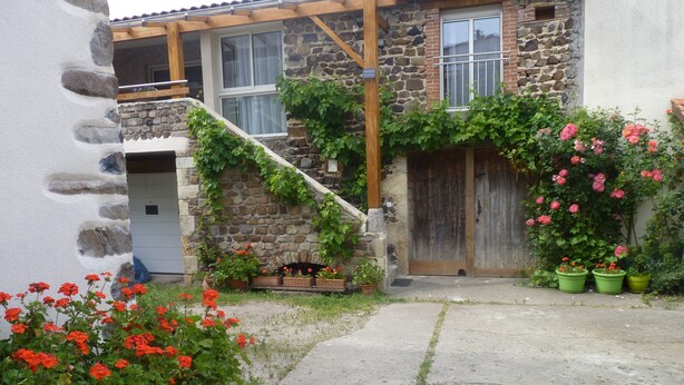 Una casa in pietra con una scala in legno, una porta di legno e vasi con fiori rossi.