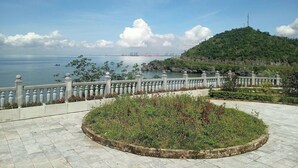 Une promenade dallée agrémentée d’une rambarde décorative, un espace paysager aménagé et une vue sur une étendue d’eau et des bâtiments industriels éloignés.