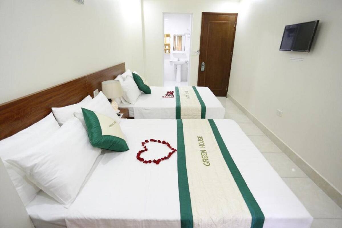 A hotel room with two beds, each with a green-striped bed runner and a heart-shaped decoration on the bed.