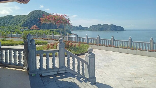 Une terrasse dallée, agrémentée d’une balustrade, qui offre une vue sur un plan d’eau et un paysage montagneux.