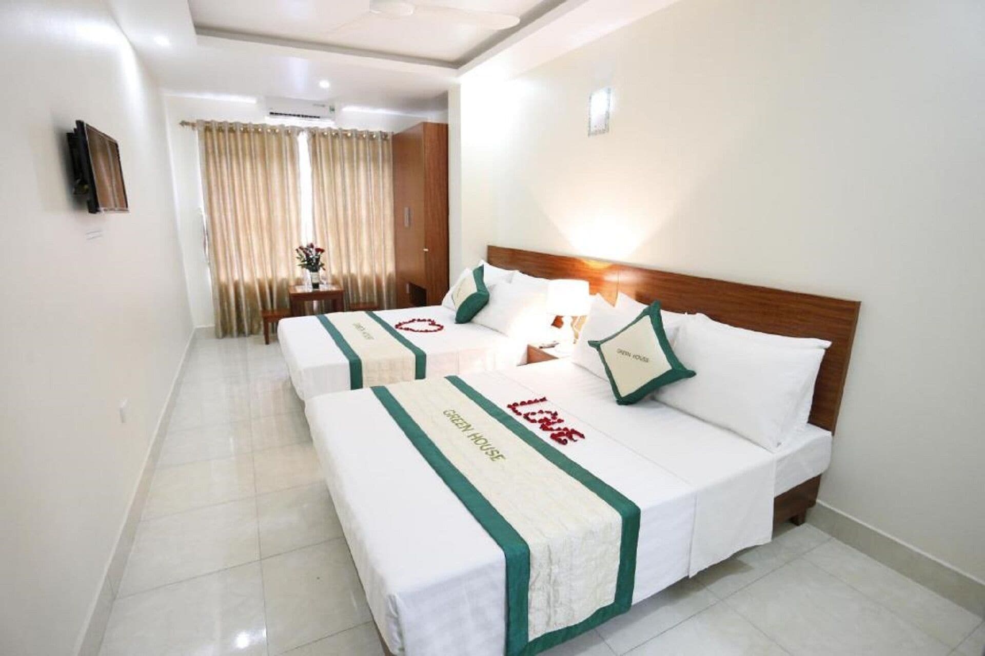 A hotel room with two beds, a wooden headboard, a small table with a lamp, and a window with curtains.