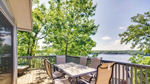 A wooden deck with a table and chairs, overlooking a lake and trees. - Lake-view Home at Margaritaville Resort! (Osage Beach)