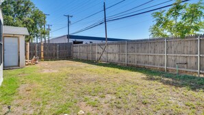 A backyard with a wooden fence, a shed, and a house in the background. - Convenient Lubbock Vacation Rental, 2 Mi to Ttu! (Lubbock)