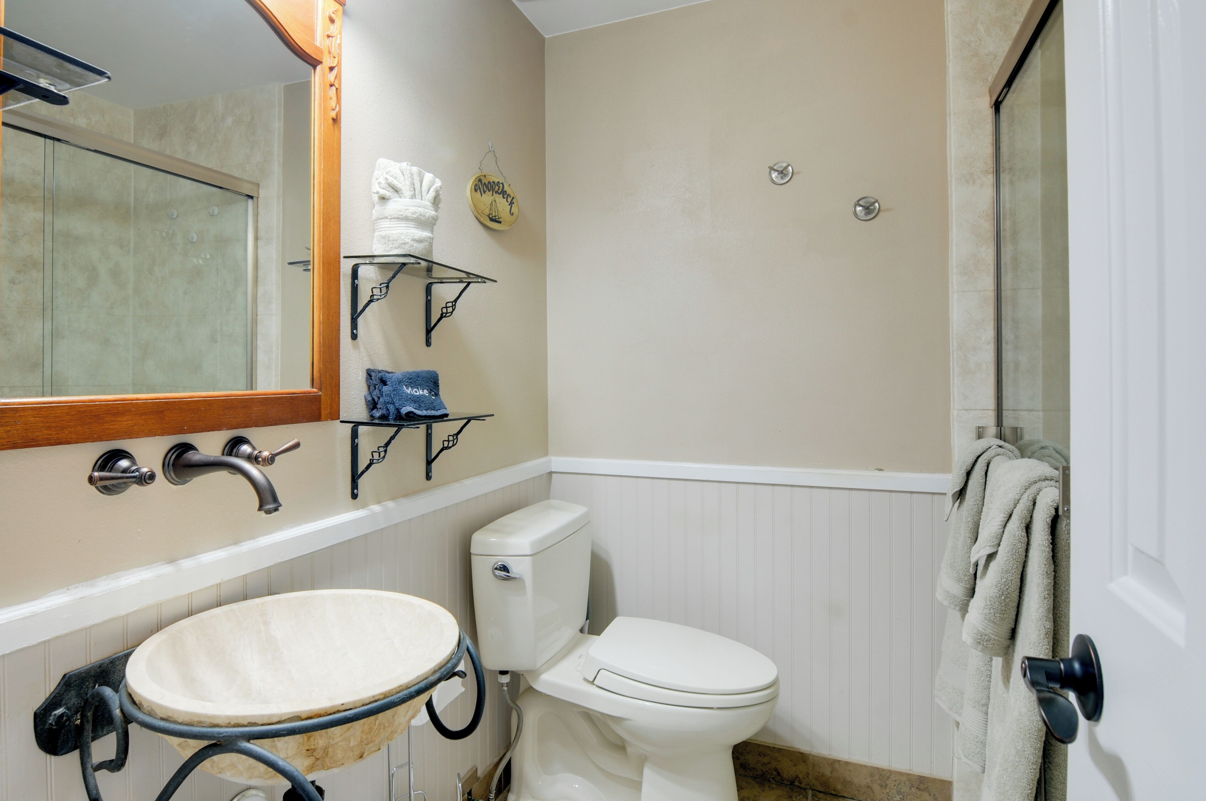 Un baño con lavamanos, inodoro y ducha. Hay toalleros y un estante con toallas.