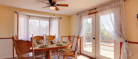 A dining area with a wooden table and chairs, a ceiling fan, and large windows with curtains.