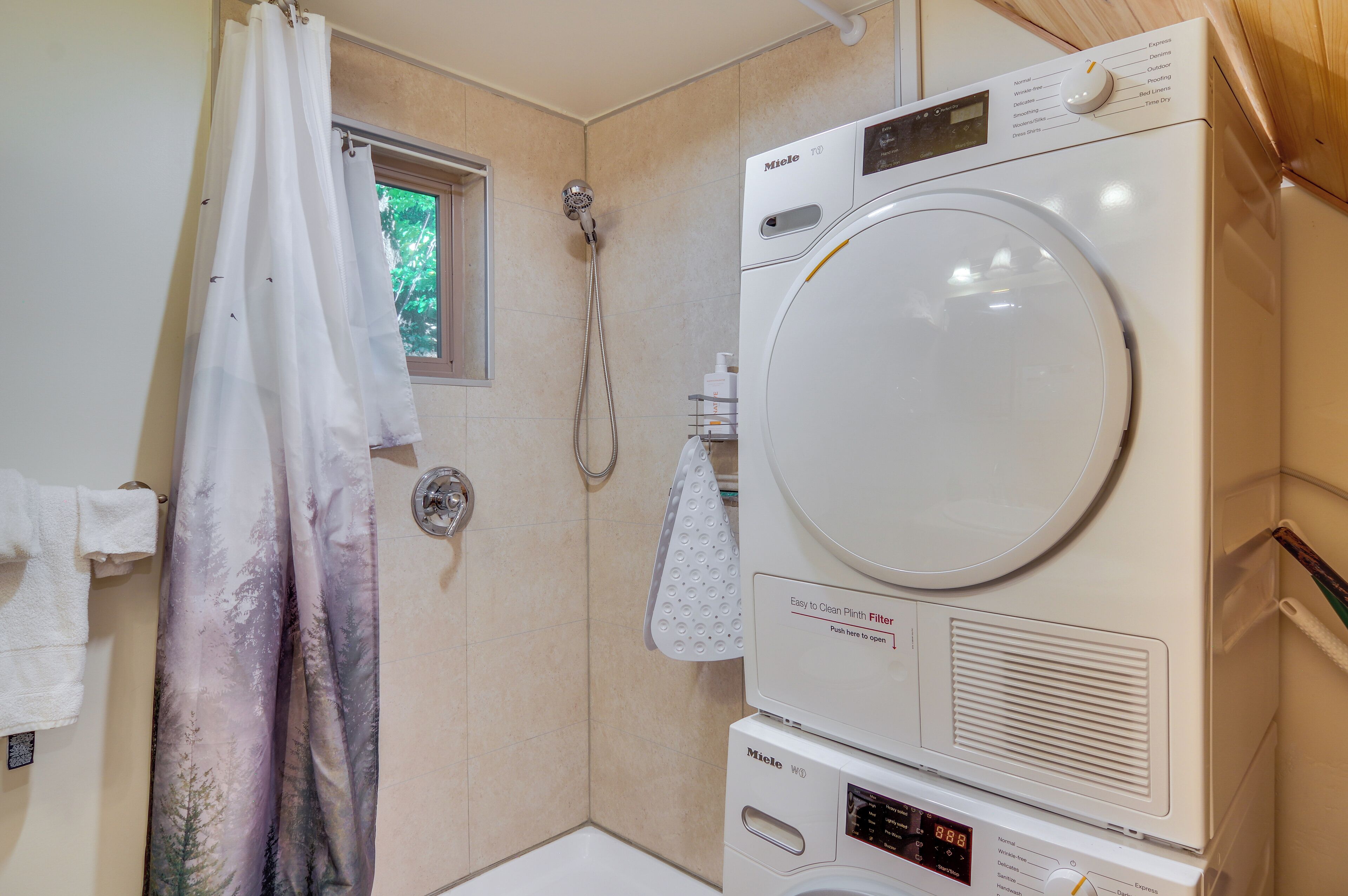 A laundry room with a front-loading washing machine, a dryer, and a shower.