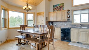 A spacious kitchen with wooden cabinets, a dining table, and chairs. There is a large window providing natural light and a view of trees. - Jefferson Mountain Cabin w/ Private Deck & Grill! (Como)