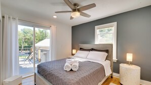 Une chambre à coucher avec un lit, un ventilateur de plafond, une table de chevet et une vue sur l’extérieur.