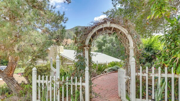 A white wooden gate with a vine-covered archway leading to a brick pathway. - Cozy Escondido Escape Near Hiking & Downtown! (Escondido)