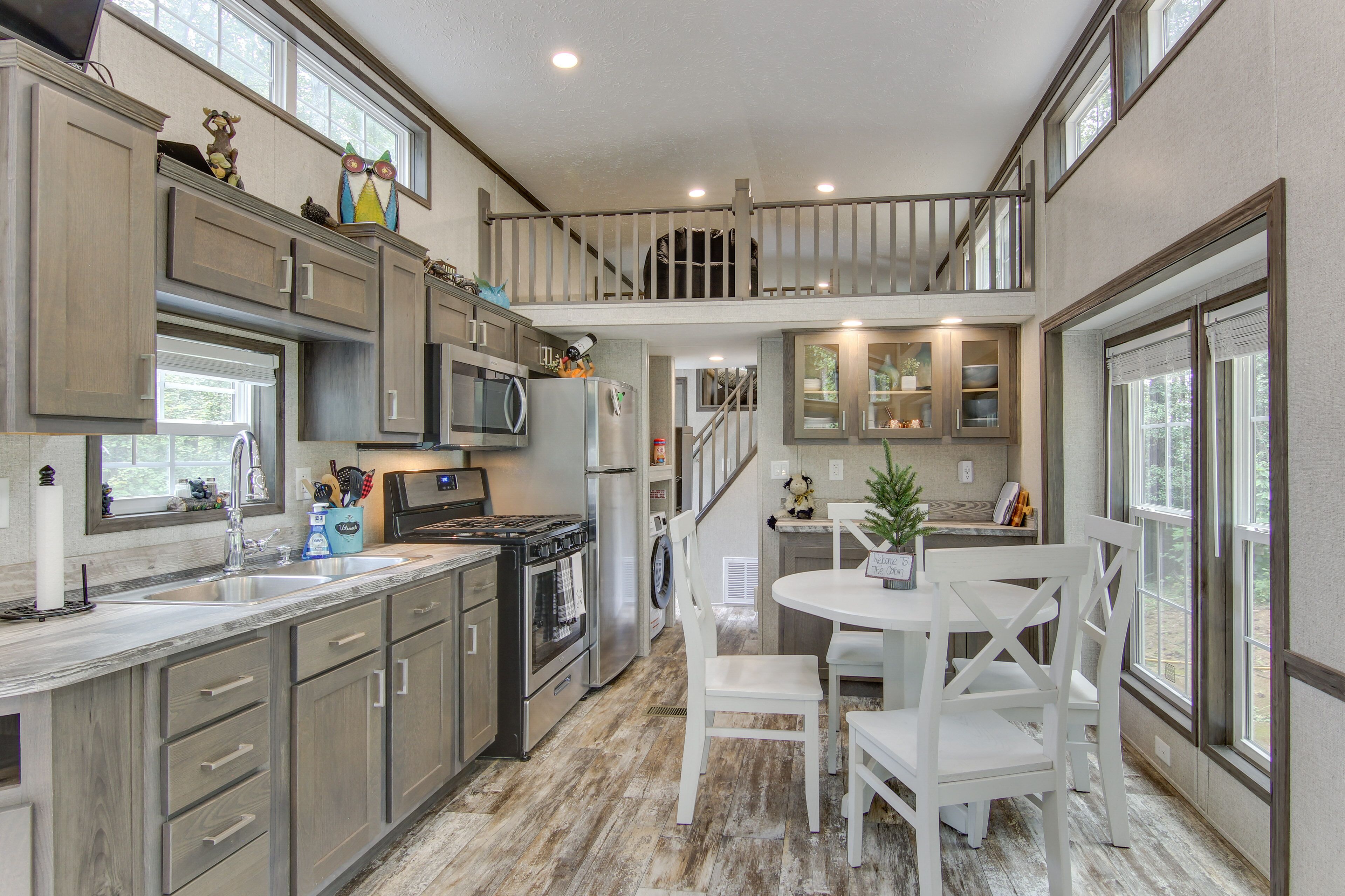 A spacious kitchen with modern appliances, a dining area with white chairs, and a view of the outdoors through large windows.