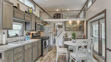 A spacious kitchen with modern appliances, a dining area with white chairs, and a view of the outdoors through large windows.