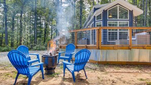 Een chalet met een vuurkuil en blauwe stoelen, gelegen in een bos.