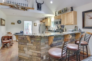 Una cocina con una isla de piedra, armarios de madera y un techo alto decorado con un cráneo de vaca.