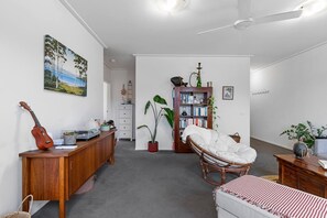 A room with a wooden desk, a guitar, a bookshelf, a wicker chair, and a bed. - Simply Kensington by Ready Set Stay (Kensington)