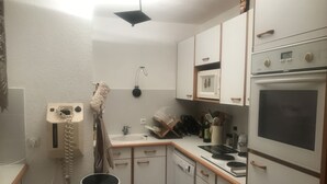 A compact kitchen with white cabinets, a microwave, an oven, and a sink. There is a hanging towel and a small trash bin.