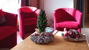 A cozy living room with two red armchairs, a small Christmas tree, and a wooden coffee table.