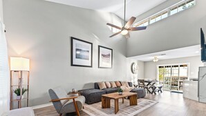 Ein großzügiges Wohnzimmer mit grauem Sofa, einem Holztisch und einem modernen Deckenventilator.