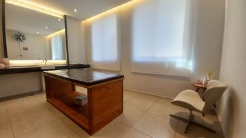 Un bagno moderno con un mobile contenitore in legno, uno specchio e una sedia bianca.