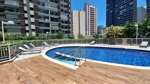 Ein Pool auf dem Dach mit Holzterrasse, umgeben von einem Metallgeländer und Liegestühlen.