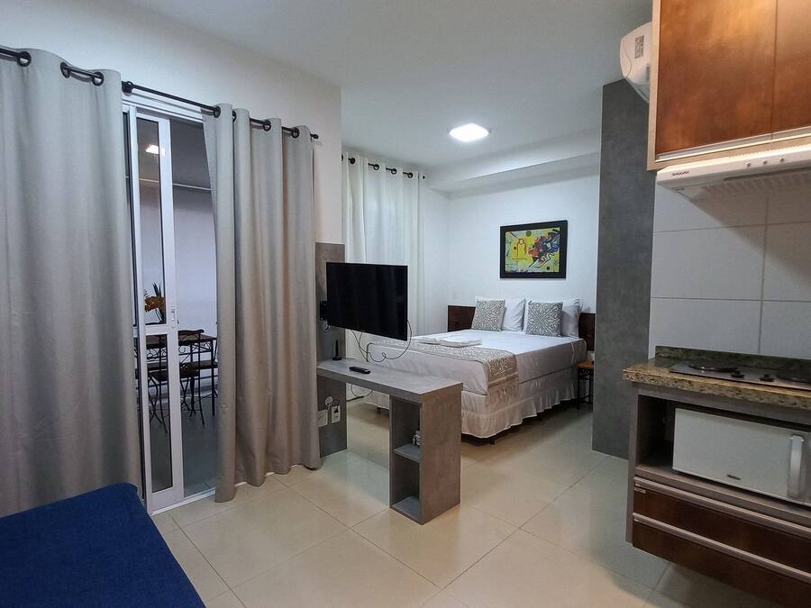 Habitación de hotel pequeña con cama, escritorio con televisor, microondas y zona de comedor con mesa y sillas.