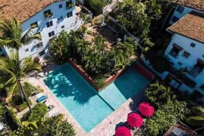Vista aérea de um hotel com piscina central, cercada por vegetação exuberante e palmeiras.